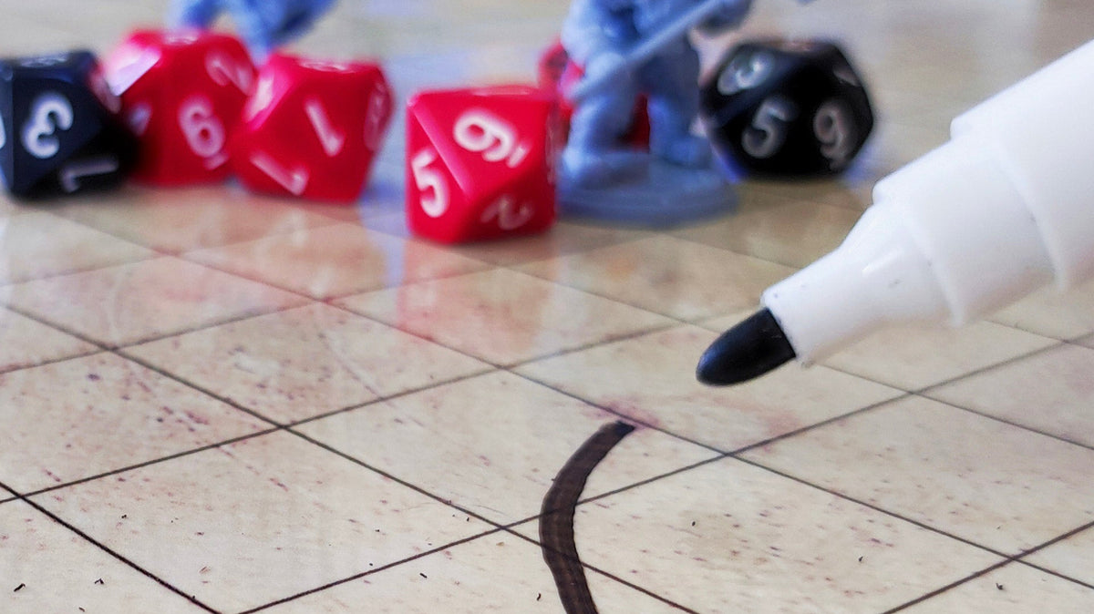 Dry-erase marker drawing a line on a gridded RPG mat, with dice and miniatures in the background.