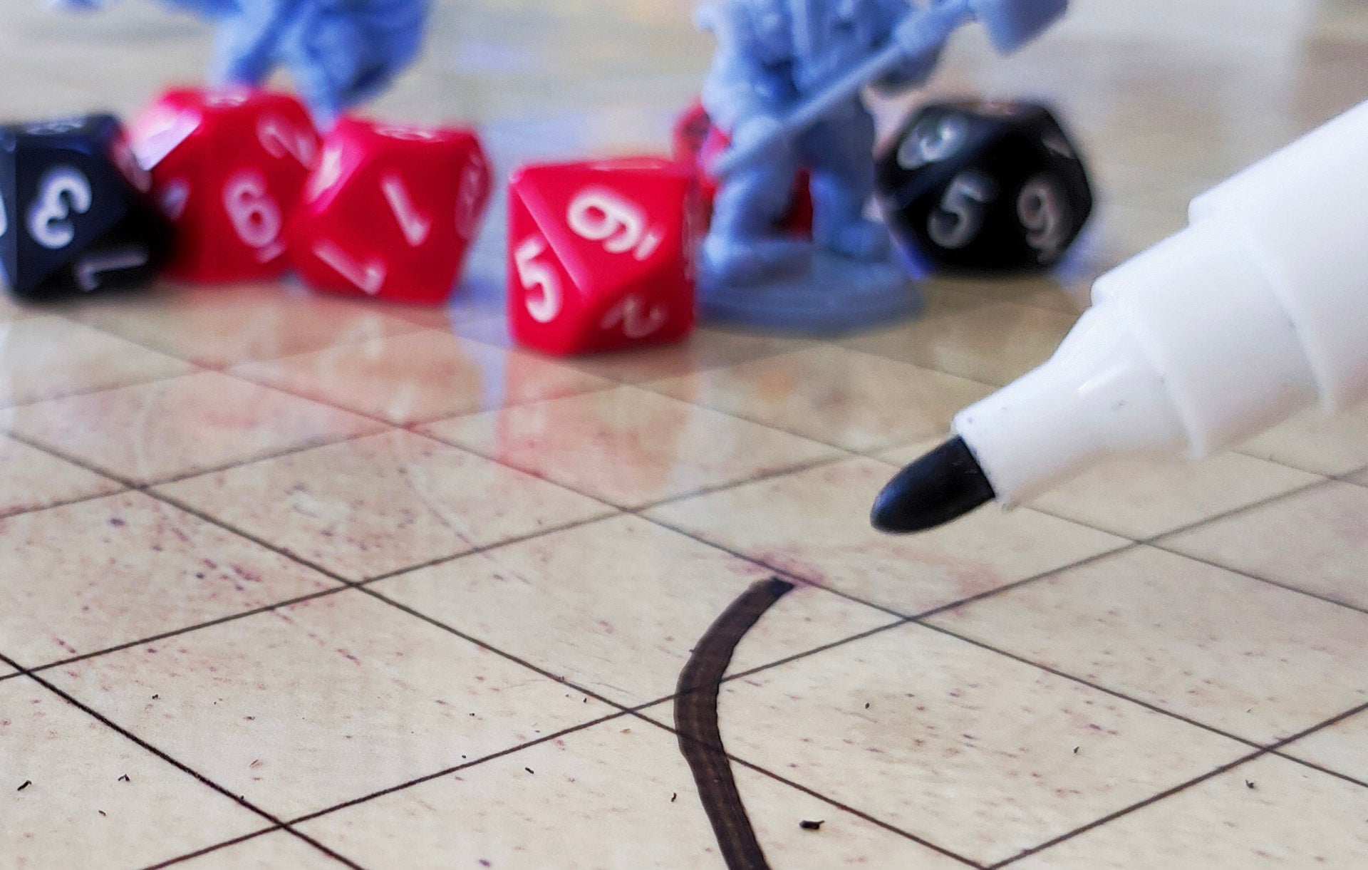 Dry-erase marker drawing a line on a gridded RPG mat, with dice and miniatures in the background.
